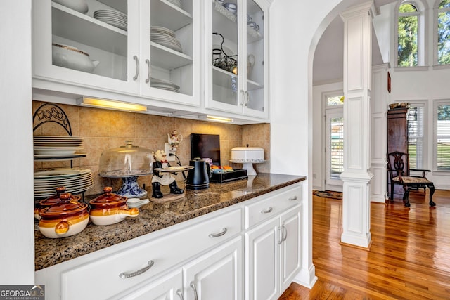 bar featuring decorative backsplash, arched walkways, light wood-style flooring, and ornate columns