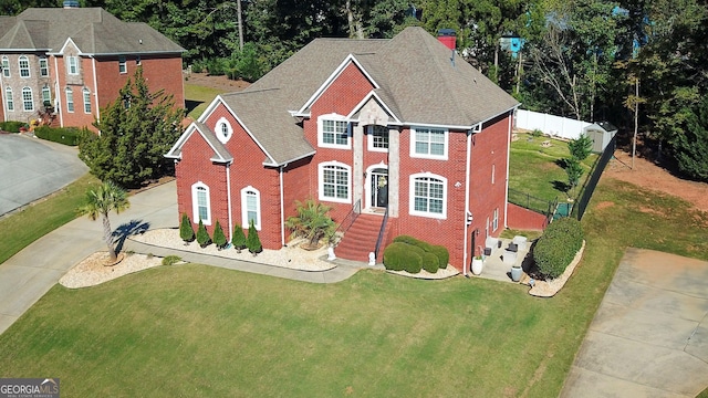 view of front of home featuring brick siding, a chimney, fence, driveway, and a front lawn