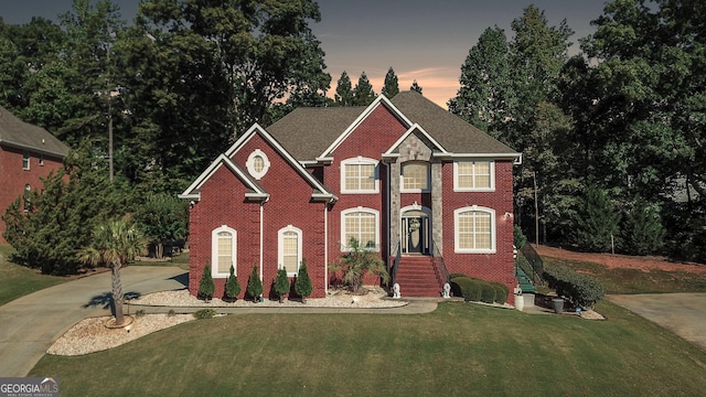 colonial inspired home with concrete driveway, brick siding, and a front lawn