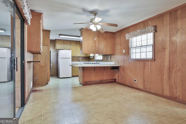 kitchen with white fridge, ceiling fan, kitchen peninsula, and wood walls