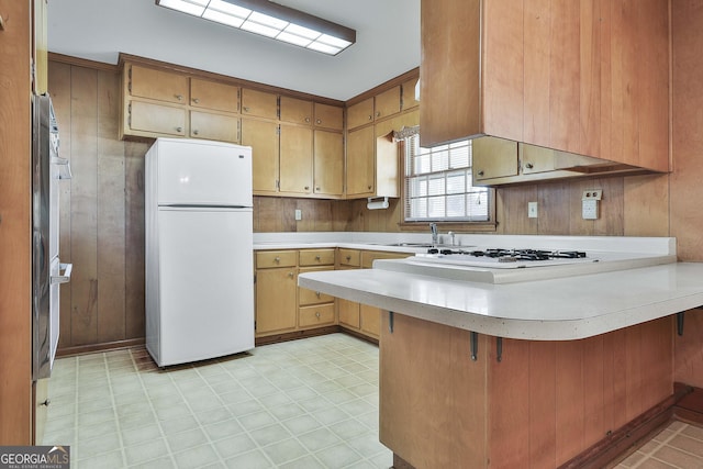 kitchen with wood walls, sink, kitchen peninsula, and white appliances