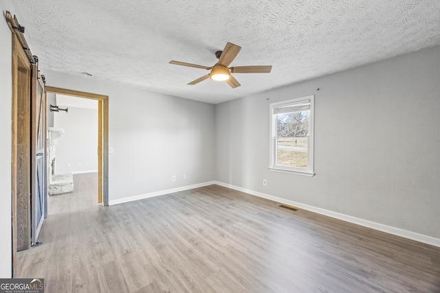 spare room with ceiling fan, a barn door, a textured ceiling, and hardwood / wood-style floors