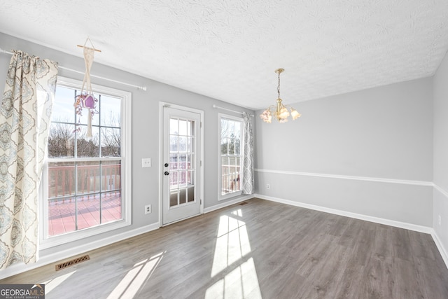 unfurnished dining area with hardwood / wood-style floors, a chandelier, and a healthy amount of sunlight