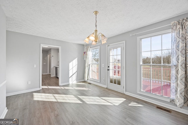 unfurnished dining area featuring an inviting chandelier, a textured ceiling, and hardwood / wood-style floors