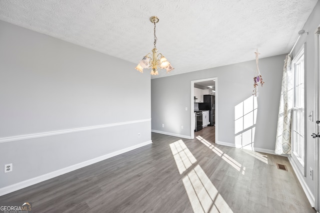 unfurnished room featuring a textured ceiling, dark hardwood / wood-style flooring, and an inviting chandelier