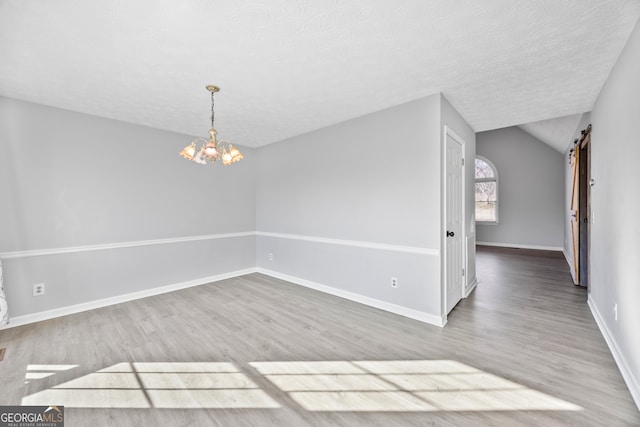 empty room with lofted ceiling, a barn door, hardwood / wood-style flooring, a textured ceiling, and a chandelier