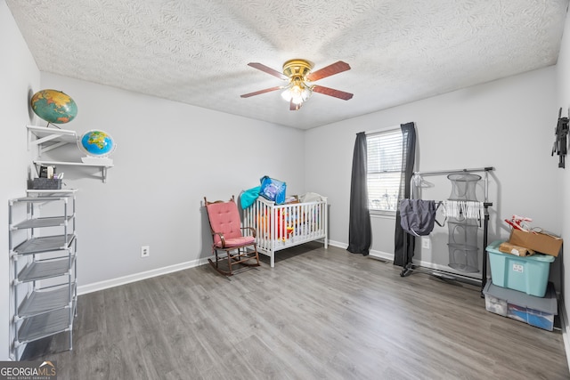 bedroom featuring a textured ceiling, ceiling fan, wood-type flooring, and a nursery area