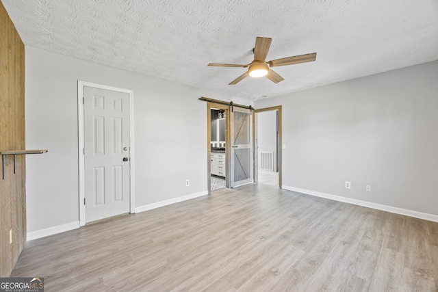 interior space featuring ceiling fan, a textured ceiling, a barn door, and light wood-type flooring