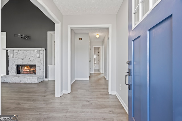 entryway with light wood-type flooring, a stone fireplace, and a textured ceiling