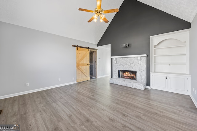 unfurnished living room featuring a fireplace, ceiling fan, built in features, high vaulted ceiling, and a barn door