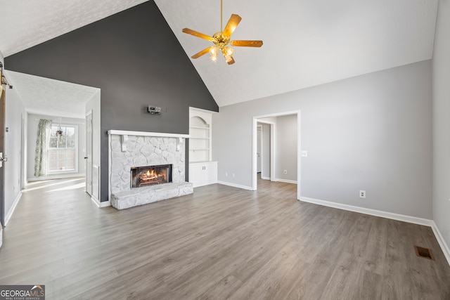 unfurnished living room featuring ceiling fan, a fireplace, hardwood / wood-style floors, high vaulted ceiling, and built in shelves