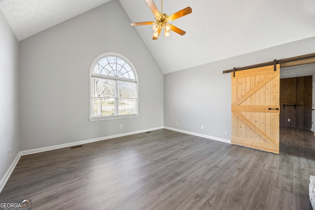 empty room with ceiling fan, a barn door, dark hardwood / wood-style floors, a textured ceiling, and high vaulted ceiling