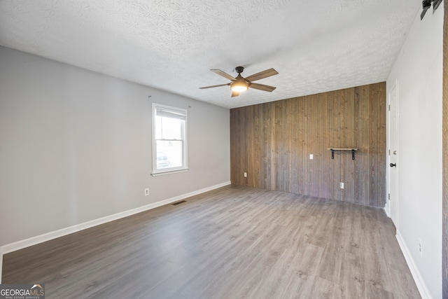 spare room with wood-type flooring, a textured ceiling, ceiling fan, and wooden walls