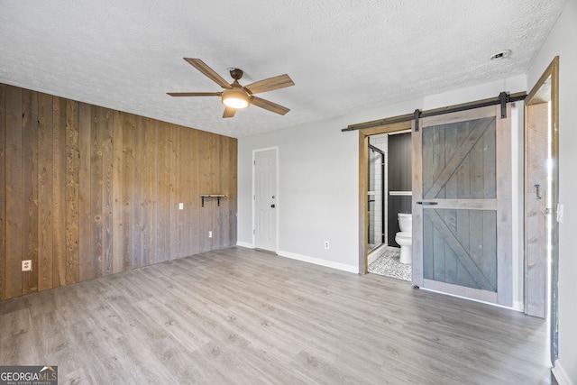 unfurnished room featuring ceiling fan, a textured ceiling, wood walls, and a barn door