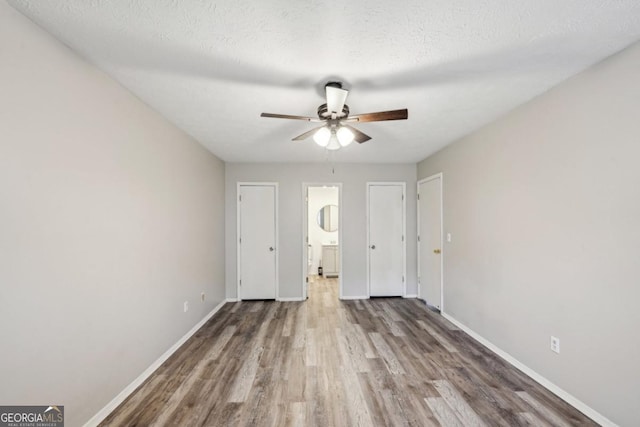 unfurnished bedroom with ceiling fan, ensuite bath, wood-type flooring, and a textured ceiling