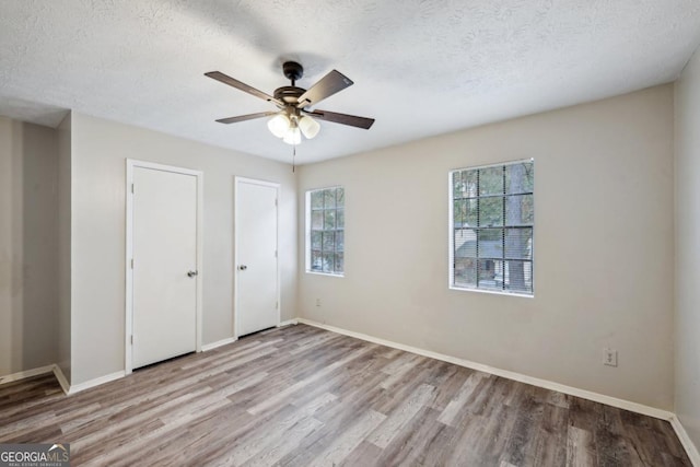 unfurnished bedroom with ceiling fan, two closets, a textured ceiling, and light hardwood / wood-style flooring