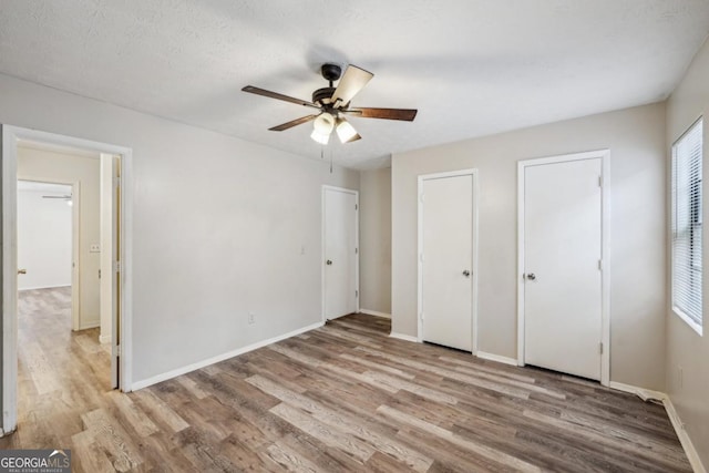 unfurnished bedroom featuring a textured ceiling, ceiling fan, two closets, and light hardwood / wood-style floors