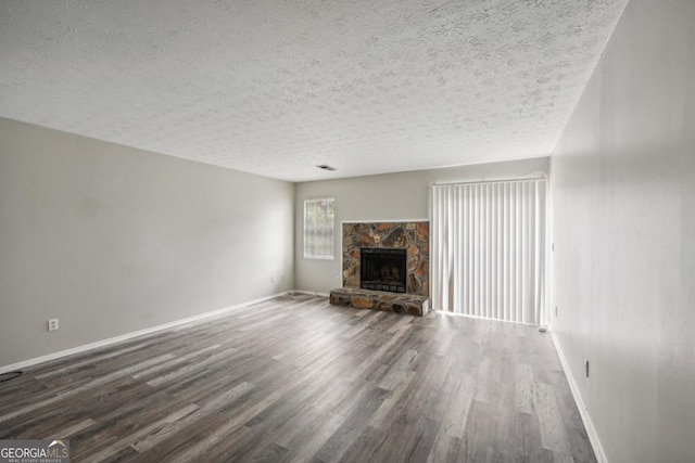 unfurnished living room with a textured ceiling, dark hardwood / wood-style flooring, and a stone fireplace