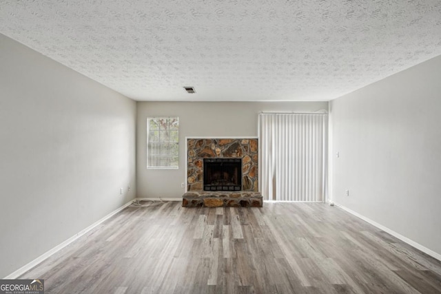 unfurnished living room with hardwood / wood-style flooring, a textured ceiling, and a stone fireplace