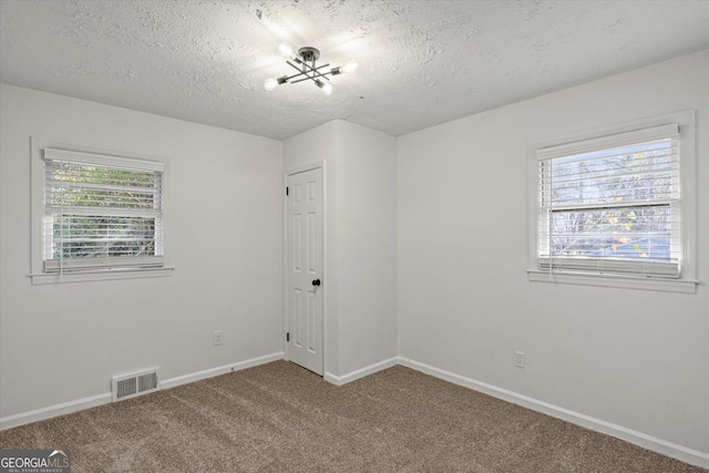 carpeted spare room with a textured ceiling and a notable chandelier