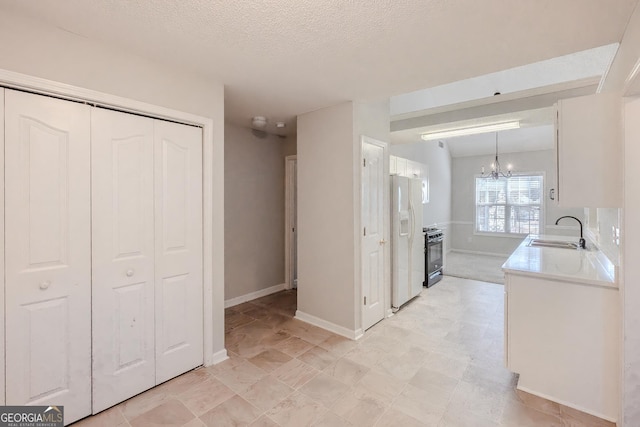 kitchen with white cabinetry, gas stove, hanging light fixtures, white refrigerator with ice dispenser, and sink