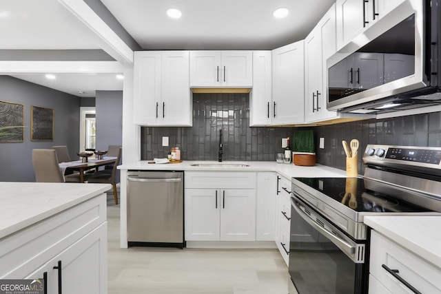 kitchen with appliances with stainless steel finishes, white cabinetry, sink, backsplash, and light stone counters