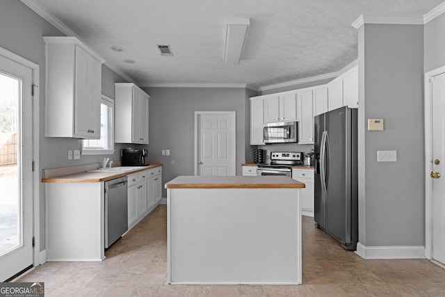 kitchen featuring white cabinetry, ornamental molding, stainless steel appliances, and a kitchen island