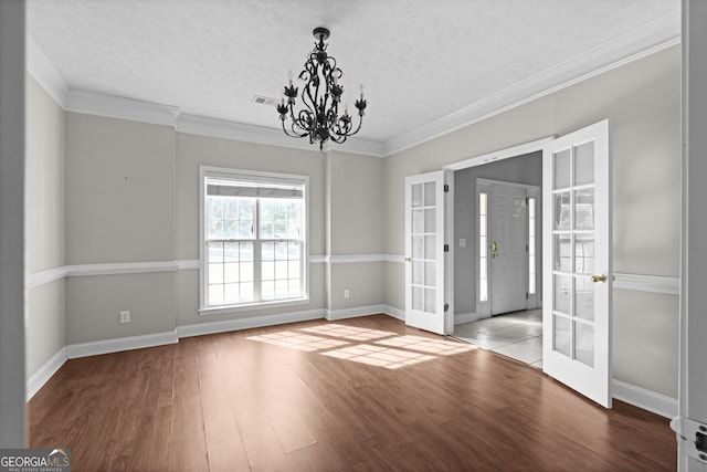 unfurnished room featuring hardwood / wood-style flooring, a chandelier, ornamental molding, and french doors