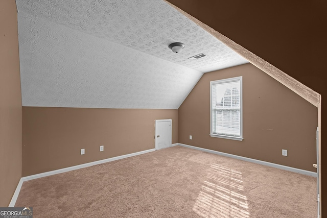 additional living space featuring a textured ceiling, carpet flooring, and vaulted ceiling