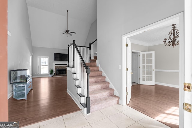 stairs with ceiling fan, tile patterned floors, high vaulted ceiling, and crown molding