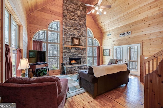 living room with wood ceiling, french doors, a stone fireplace, ceiling fan, and high vaulted ceiling