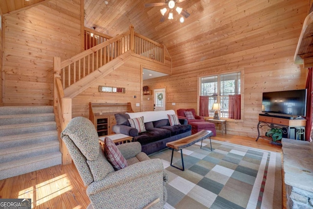 living room with high vaulted ceiling, ceiling fan, wood walls, and light hardwood / wood-style floors