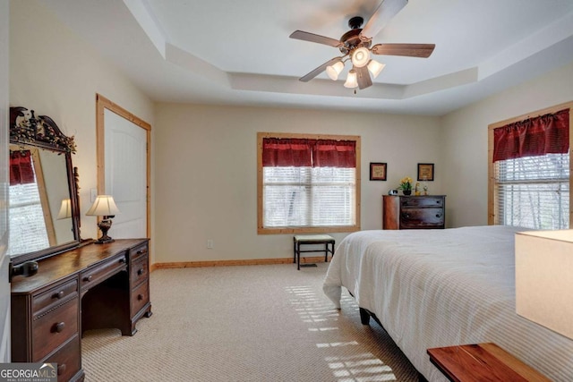 carpeted bedroom with ceiling fan and a raised ceiling