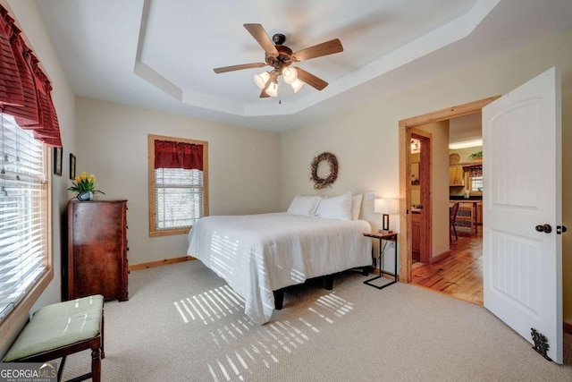 bedroom with ceiling fan, light colored carpet, and a tray ceiling