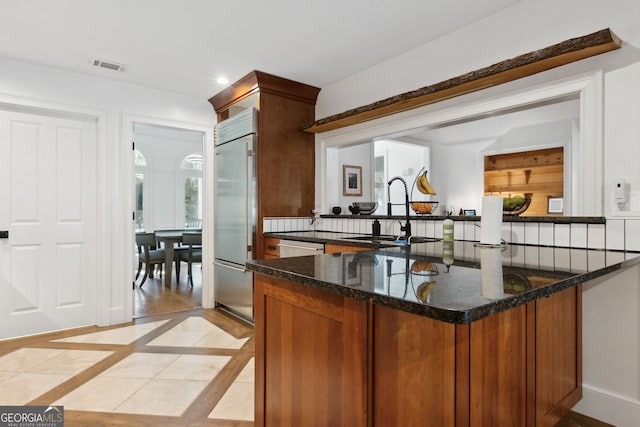 kitchen with dark stone countertops, kitchen peninsula, sink, light tile patterned floors, and built in fridge