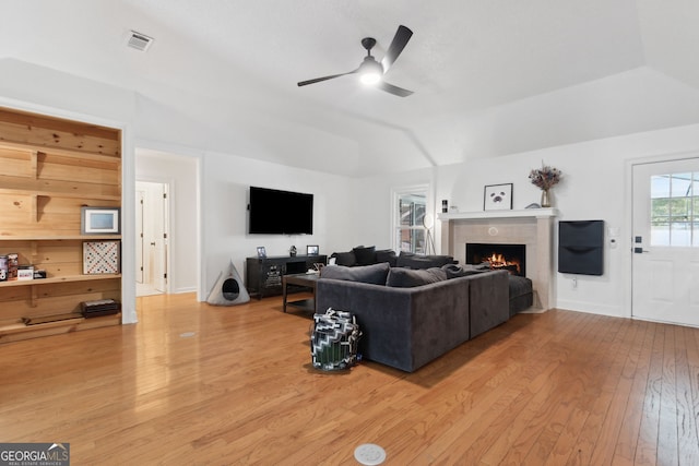 living room featuring vaulted ceiling, ceiling fan, a tiled fireplace, and wood-type flooring