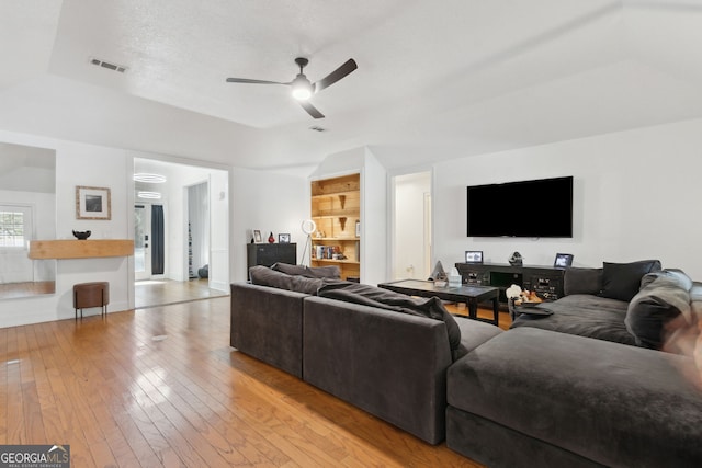 living room with a textured ceiling, ceiling fan, light hardwood / wood-style floors, and a raised ceiling