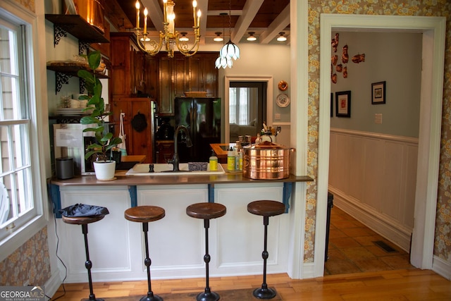 kitchen with black refrigerator with ice dispenser, sink, light hardwood / wood-style flooring, hanging light fixtures, and a breakfast bar area