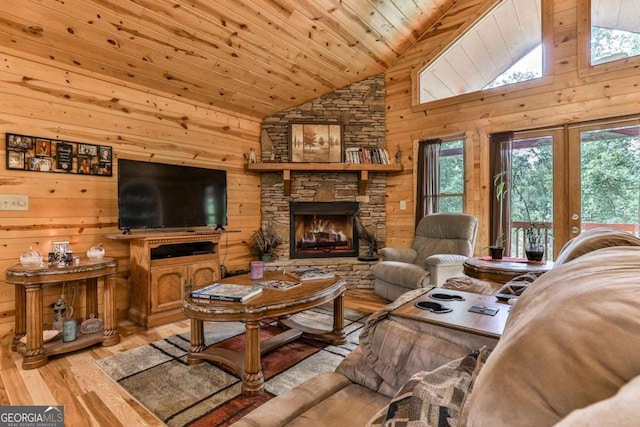 living room featuring wood walls, light hardwood / wood-style floors, wood ceiling, a stone fireplace, and high vaulted ceiling