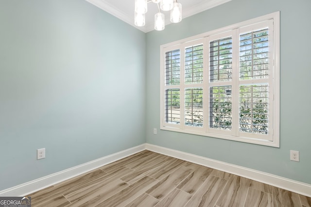 empty room with ornamental molding, a notable chandelier, baseboards, and wood finished floors