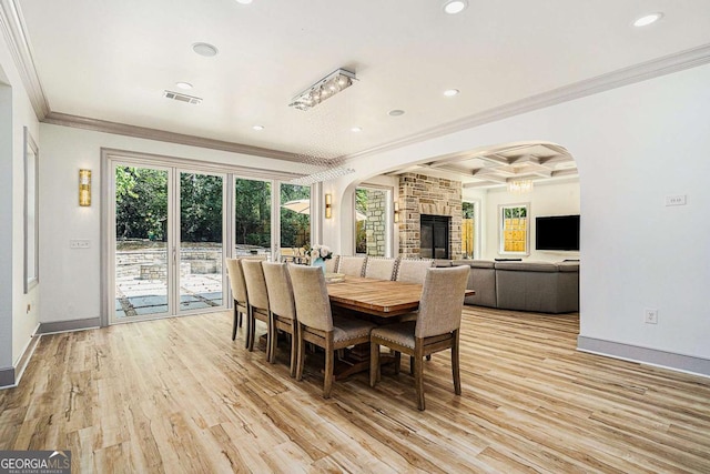 dining room featuring coffered ceiling, a stone fireplace, light wood-type flooring, ornamental molding, and beamed ceiling