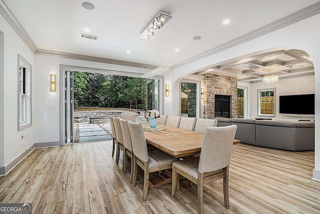 dining room featuring beam ceiling, crown molding, coffered ceiling, light hardwood / wood-style flooring, and a stone fireplace