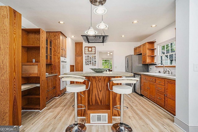 kitchen featuring appliances with stainless steel finishes, light hardwood / wood-style floors, a kitchen breakfast bar, hanging light fixtures, and sink