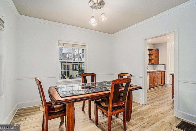 dining area with ornamental molding and light hardwood / wood-style floors