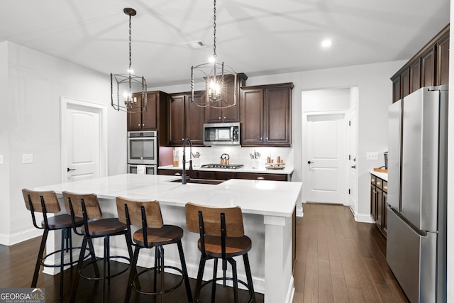 kitchen with appliances with stainless steel finishes, dark hardwood / wood-style floors, hanging light fixtures, a kitchen island with sink, and tasteful backsplash