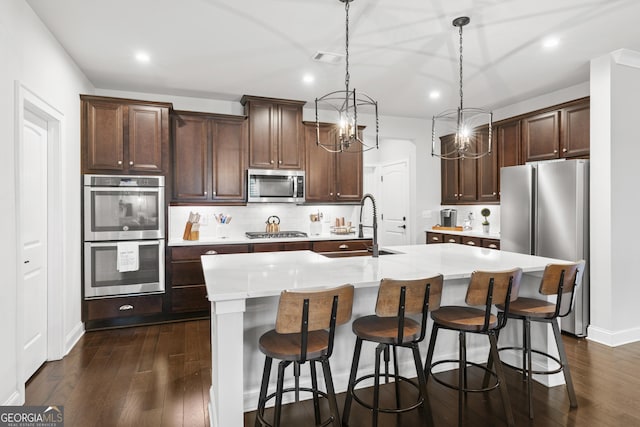 kitchen featuring a center island with sink, hanging light fixtures, dark brown cabinets, stainless steel appliances, and sink