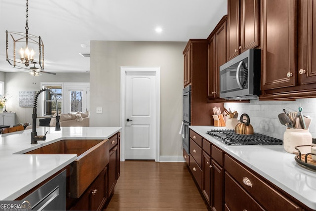 kitchen with a sink, backsplash, dark wood-style floors, appliances with stainless steel finishes, and light countertops