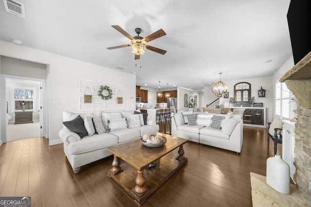 living area featuring dark wood finished floors, ceiling fan with notable chandelier, and visible vents