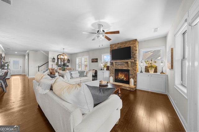 living area with visible vents, ceiling fan with notable chandelier, dark wood finished floors, a fireplace, and stairs