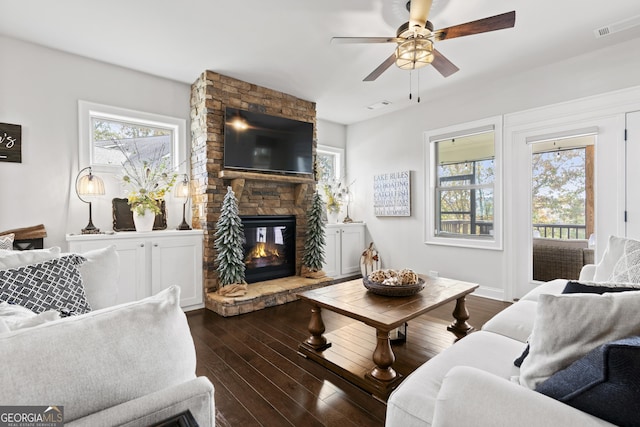 living room featuring a stone fireplace, dark hardwood / wood-style floors, and a healthy amount of sunlight